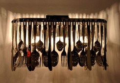 alt: struttura base della lampada metallica in cromo lucido decorata da forchette, cucchiai e coltelli in acciaio inox