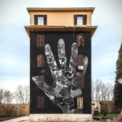 mural colorato sull’intera facciata della palazzina che rappresenta su sfondo nero una mano gigante sulla cui superfice vi sono motivi grafici in bianco